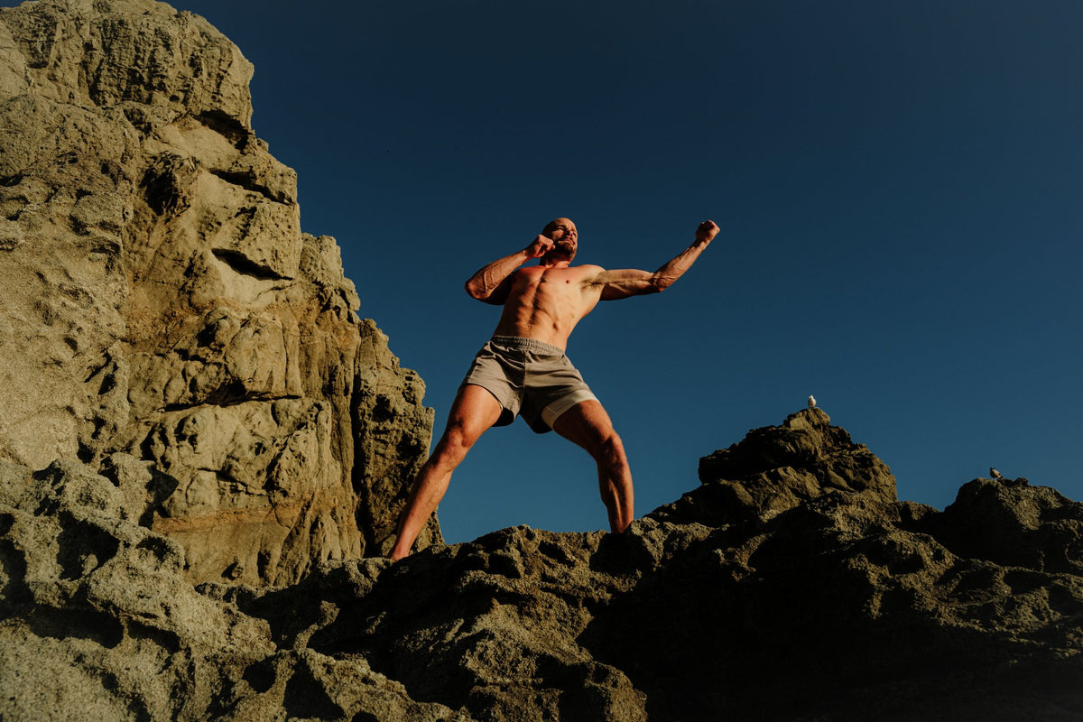 A figure reaching skyward on the rocks above the ocean